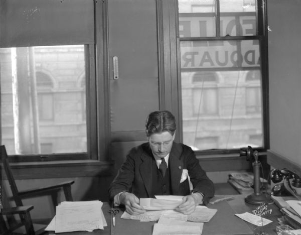 Governor elect Philip La Follette sitting and reading a telegram at La Follette headquarters.