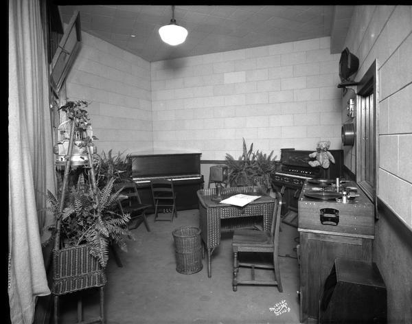 WIBA fern room with piano, organ, ferns, and a turntable. There is a Teddy Bear on top of the organ on the right, and on the left is a bird in a birdcage.