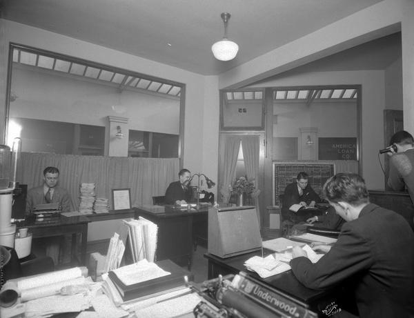 WIBA office, with four men working at desks. There is an Underwood typewriter in the foreground.