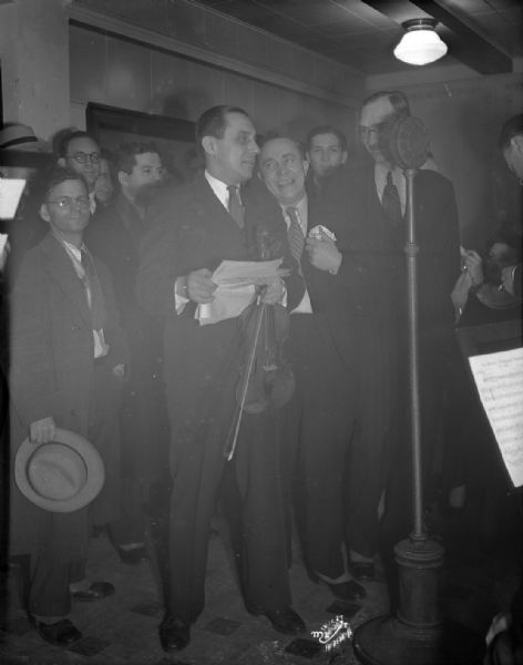 Ole Olsen & Chic Johnson at WISJ radio station in front of microphone, with one of them holding a violin. John Sharnberg, manager of Orpheum Theatre is standing between Olsen and Johnson. This was a benefit for the Empty Stocking Fund.