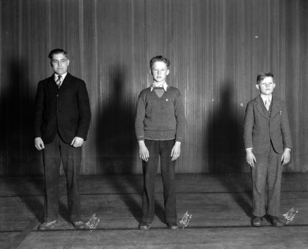 Three male cheerleaders on East High School stage. Beside each person are, left to right, the numbers: 2100B-1, 2100B-2, 2100B-3 = Harb.