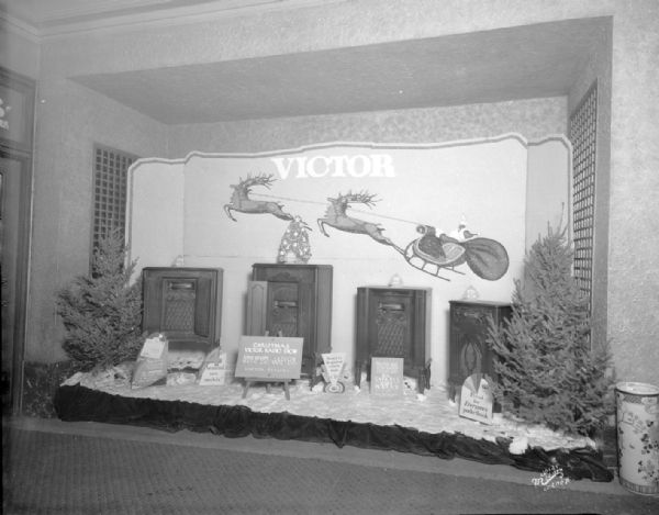 Christmas Victor radio show display in Orpheum theater lobby. There are four console radios and two Christmas trees. On the wall is a depiction of Santa in a sleigh pulled by reindeer.