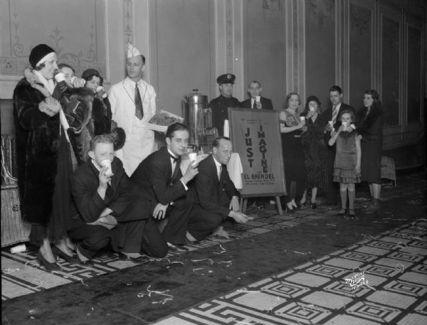 Group of people drinking coffee and being served donuts on New Year's Eve at the Strand Theater. In the center is a sign for the "Just Imagine" movie.