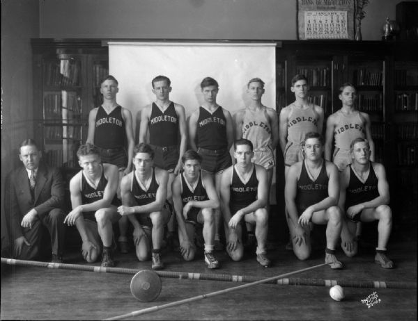 Group portrait of Middleton High School boy's track squad in uniform, including the coach. There is a pole vault and discus in the foreground.