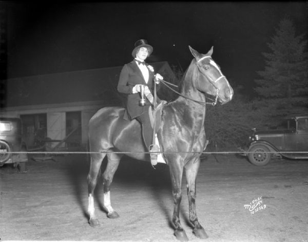 Mrs. Mary K. Holt of Blackhawk Riding Academy sitting on a horse named "Flying Squirrel," owned by Frances Edmondson. She is holding the trophy she won in the Three Gaited Open, at the 1931 Little International horse show.