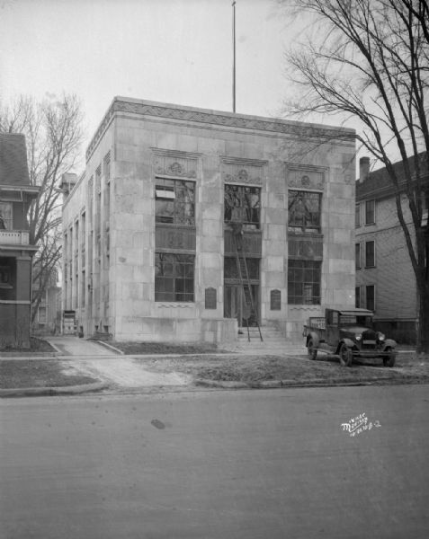 Holstein-Friesian Association of America building, 448 W. Washington Avenue. There is a truck parked on the terrace, and a man is on a ladder in front of the entrance that is reaching up to the second-story windows.