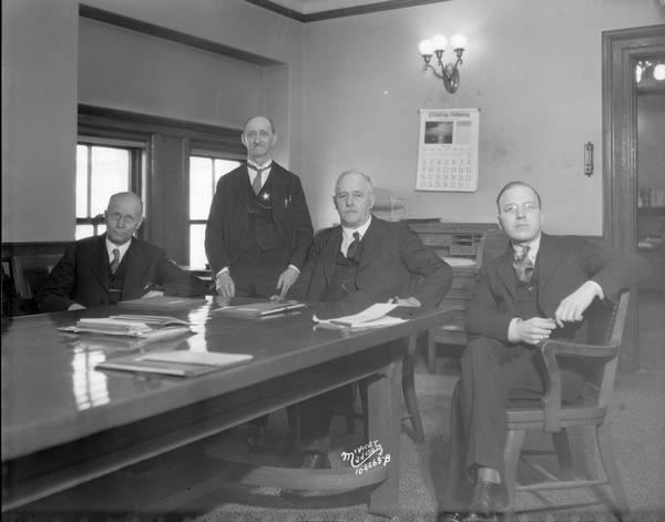 Seated L to R: Senator Herman J. Severson, Senator Walter S. Goodland, chairman of the committee, and Oliver Knutson, clerk of the committee. Standing is Emil Hartman, Senate sergeant-at-arms and not a member of the committee. This special committee investigated the charges of Senator Peter J. Smith that an effort had been made to influence his vote on utility legislation.