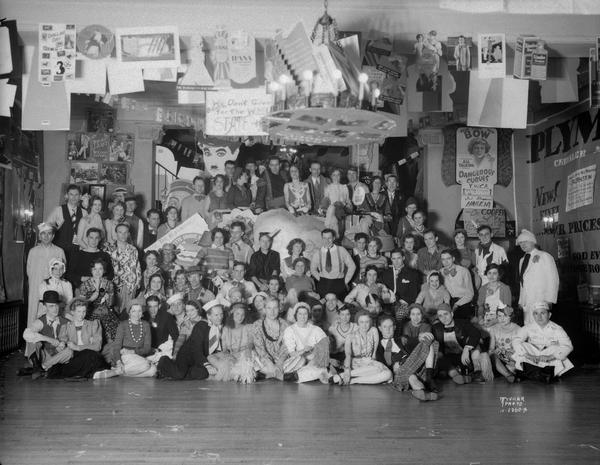 Group portrait of the Acacia fraternity "Nut House" party. Students are wearing costumes, and the room is decorated with posters.