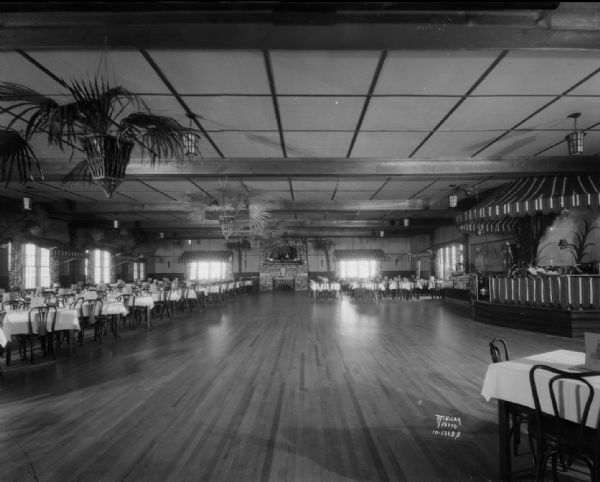 Interior of the Chanticleer Ballroom showing bandstand, dance floor and tables. There is a large stone fireplace on the far back wall. Corner of Airport Road and Highway 12.