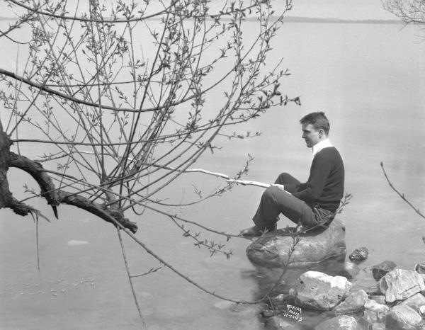 Portrait of Harold Hansen, sitting on a rock in Lake Mendota. He is holding a tree branch.