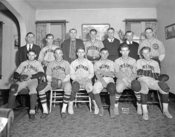 Group portrait of H.W. Simon baseball team in uniform, standing and sitting indoors.