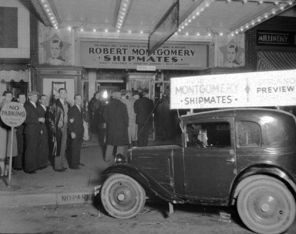 View of the front of the Strand Theatre, showing people in line to enter. There is a car with a sign on the roof that is advertising "Shipmates." 16 E. Mifflin Street.