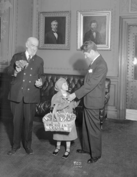 Gov. Philip La Follette buying two poppies from Jesse S. Meyers, custodian of G.A.R. Memorial Hall, representing Veterans of Foreign Wars, and Rosemary Entringer, representing the American Legion.
