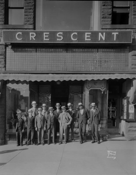 Wan Wan San Chinese acrobats and Harris and Van, from the Orpheum Theatre, wearing straw hats, in front of Crescent Clothing Store, 27 N. Pinckney Street. Also shows the Reierson' Studio.