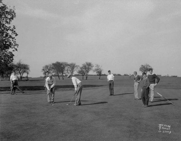 View of grade school championship golf match on the 4th green, with seven men and boys on the fourth green of Glenway Municipal Golf Course, corner of Speedway Road and Glenway Street.