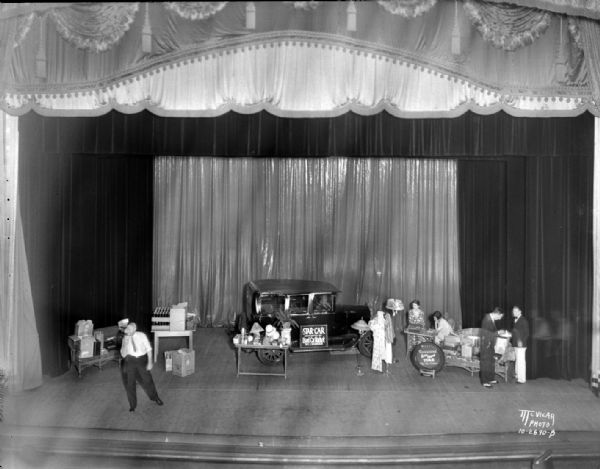 View from balcony of an auction for Kiddie Camp at the Orpheum theatre, with an automobile on the stage.