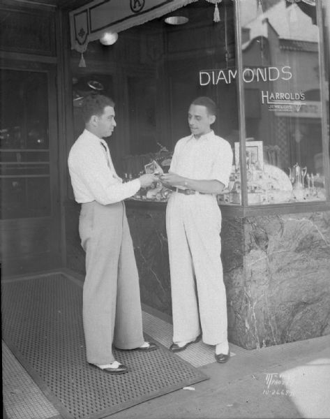 Harold Kohen, President of Harrold's Inc., jewelers, handing one of three watches he is contributing to Kiddy Camp auction, to Stephen Olsen, a brother of Ole Olsen in the Olsen and Johnson Comedy team. They are standing in front of Harrold's Jewelry store, 220 State Street.