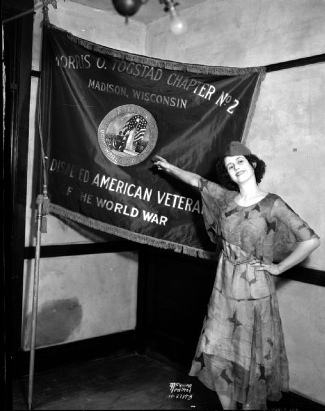 Evelyn Noll, contestant for Aviation Ball queen, pointing to Morris O. Togstad Chapter No. 2 Disabled American Veterans of the World War flag.