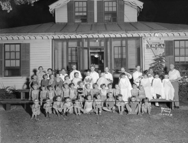 Eight barbers (S.R. Ashby, E.A. Sorenson, Louis H. Topp, Melvin Byom, Earl G. Carver, Melvin H. Randall, Joseph Fedele, and Claude E. Dyer) cutting hair of 37 children at YWCA Kiddie Camp.