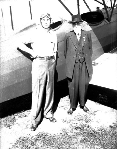 John Siggelko, age 90, and pilot Louis Wuilleumier standing in front of the airplane that took Mr. Siggelko for a ride over Madison and his old farm home about a mile and a half northeast of McFarland.