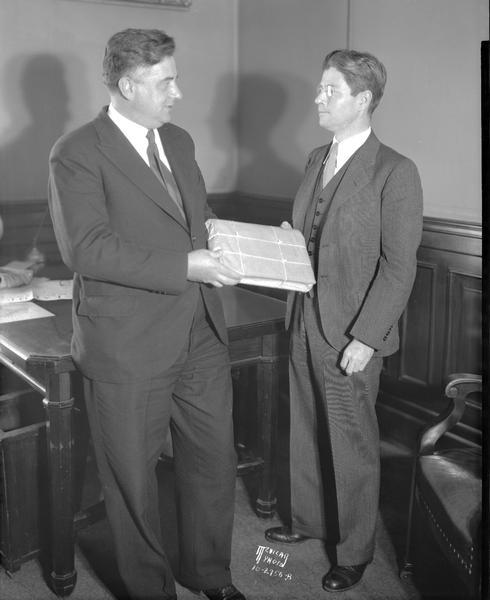 Governor Robert La Follette accepting court case documents from Milwaukee County District Attorney, George A. Bowman. The documents are the transcripts from the hearings on the affairs of the defunct Franklin State Bank, Milwaukee.