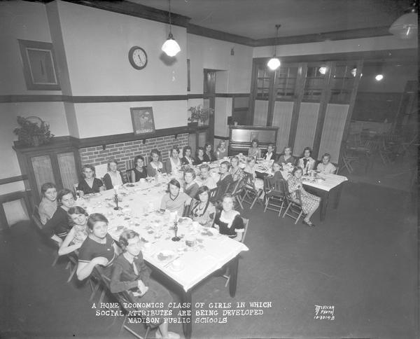 Elevated view of a Home Economics class of girls in which social attributes are being developed, Madison Public Schools, Emerson School. The girls are sitting at tables.