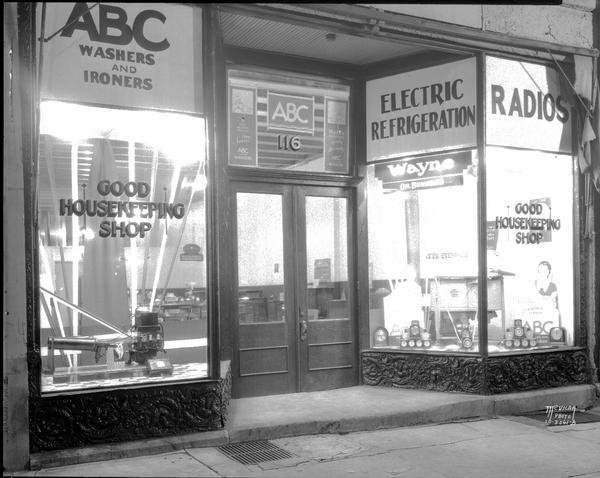Appliance store exterior featuring Wayne oil burner window display. Signs on window read: "Good Housekeeping Shop," and signs above the windows read: "ABC Washers and Ironers," "Electric Refrigeration" and "Radios." The address is 116.