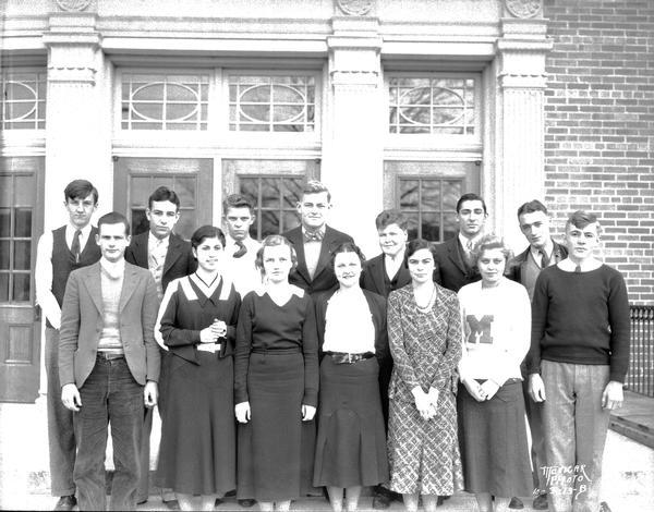 Group portrait of the play cast posing on the front steps of the school.