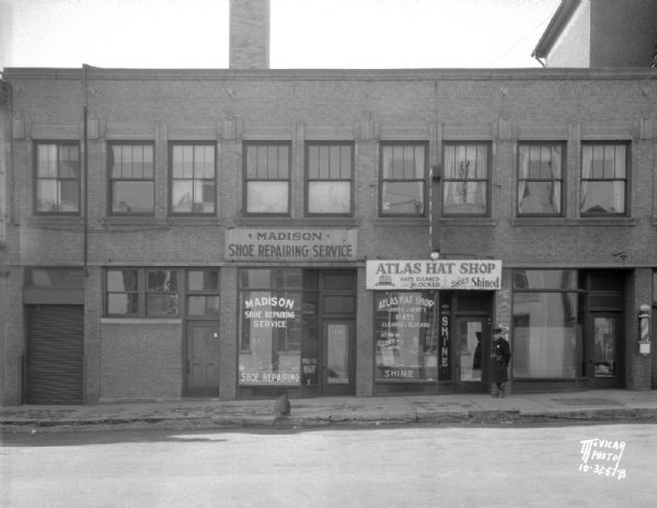 S. Pinckney Street side of S.S. Kresge Variety Store, 25 E. Main Street from second building to freight door. Also shows a barber pole at John Gay Barber, 106 S. Pinckney Street, Atlas Hat Shop, 108 S. Pinckney Street, Madison Shoe Repairing Service, 110 S. Pinckney Street, and a freight door.