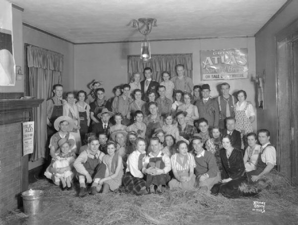Group portrait of Triangle fraternity "farm" party. On the wall in the background is an advertising sign for Atlas Special Brew.