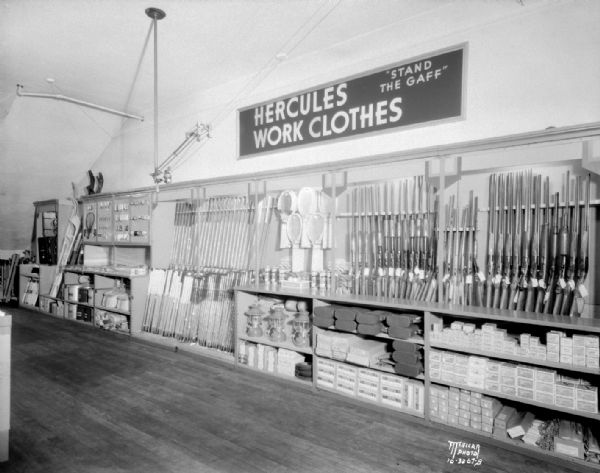 Sears Roebuck & Co. sporting goods display, featuring guns and golf clubs with "Hercules Work Clothes" sign.
