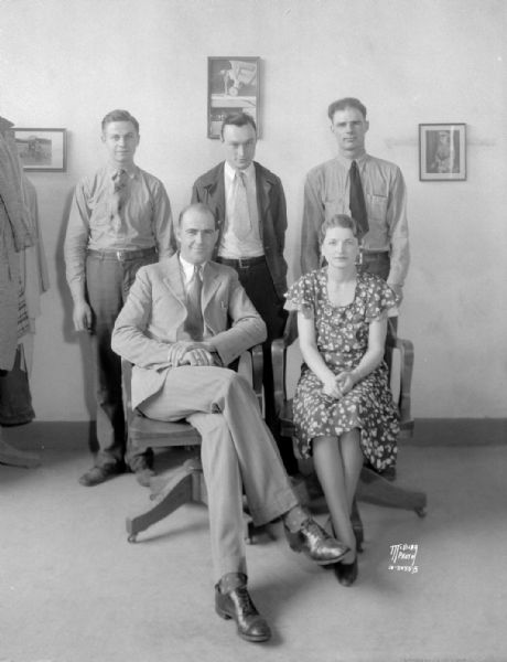 Group portrait of Morey Airplane Co. personnel, with five people. Standing left to right: Winston Smith, mechanic, Frank McCormick, pilot and shop super, Al Volk, mechanic; sitting are: Capt. Howard A. Morey, owner and proprietor, and Hazel Jacobson, bookkeeper.