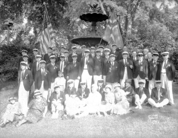 Group portrait of uniformed members of the Bjorgvin Singing Society of Chicago, most of whom were born in Bergen, Norway, taken in front the Centennial Fountain at the Executive Residence, 130 East Gilman Street. The singers had participated in a Sangerfest and memorial services for Ole Bull in the Ole Bull room in the Residence. Erected in the Capitol Park in 1878, the fountain was moved to the Governor's Mansion in 1912.