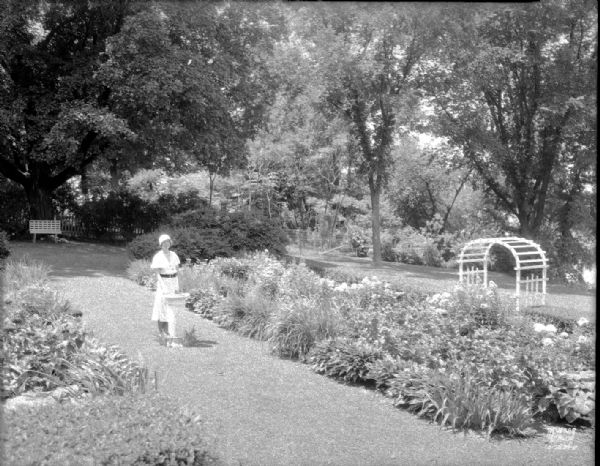 Elevated view of Vera Ford standing beside a sundial in her garden at 843 Farwell Drive.