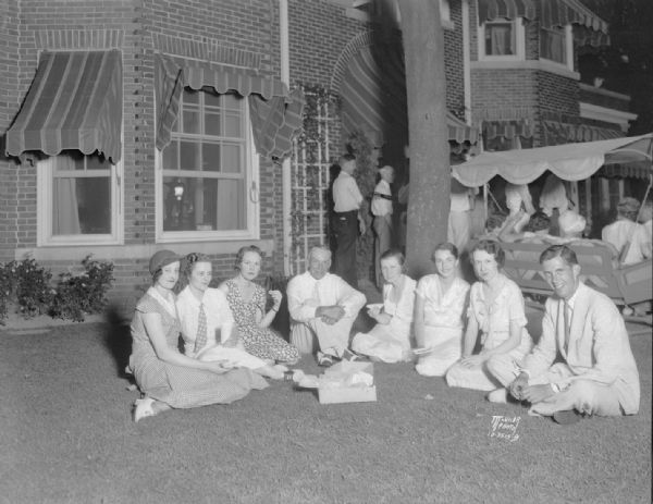 Harry and Morgan Manchester, and six girls employed at Manchesters, enjoying a picnic supper on the lawn of their Maple Bluff home. L to r: Catherine Alberti, Dorothy Ellis, Marion McPhee, Harry S. Manchester, Cornelia "Cuddy" Michaelson, Lenore Tippergrath, Catherine Jennings, and Morgan Manchester.