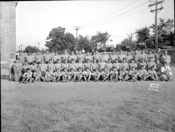 Group portrait of the West High School football squad in uniform taken outside. Also shows houses at 1 S. Vista Road and 2301 Regent Street.