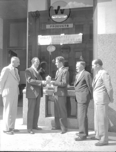 Westinghouse representive, Charles Doctal, presenting trophy to Richard H. Puelicher, D S Stophlet salesman for winning a 60 day refrigerator sales contest. Taken in front of the D S Stophlet, Inc., a Westinghouse products dealership, 114 E Main Street. L to R: Henry Czech, sales manager, Western Electric & Supply Co., Milwaukee; Charles Doctal, Richard Puelicher, Donald S. Stophlet and James P. Hagerty, Manager, local Western Electric offices.