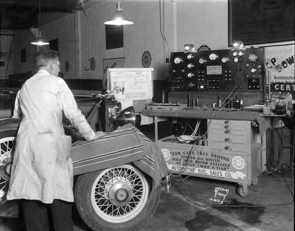 Weidenhoff Motor Analyzer, portable testing bench connected to motor of automobile, with mechanic present, at Automotive Electric Sales Co., 754 E. Washington Avenue. Sign on machine reads: "For care free driving, summer and winter, have your motor analyzed at least twice a year."