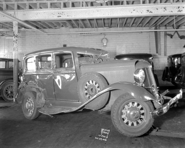 View of the passenger side of a wrecked DeSoto automobile sitting in a garage.