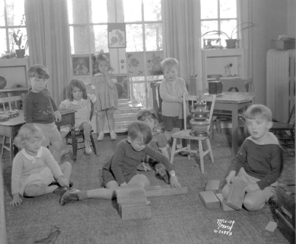 Eight children in play group at the Roy H. and Marjorie Deakman home, 7 Bayside Drive, Maple Bluff. The children are Dorothy Montague, in the chair at the left, Martha Nesbit, standing at the center back, Howard Herschleder standing near the rear, Andy Maller with his light bobbed hair, Greta Brockhausen, sitting at the left, Mary Elizabeth Schmidt, peering from behind Billy Sprague, and Tommy Hefty, sitting at the right.