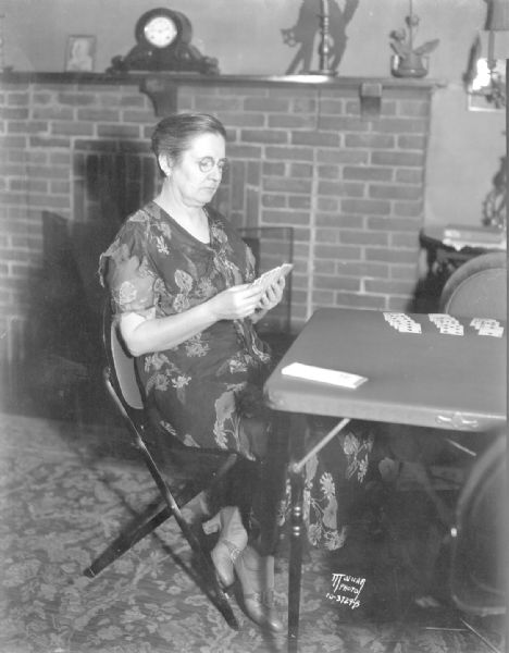 Cecily Weaver is sitting at a card table holding bridge cards. She was in charge of the "Capital Times" free contract bridge classes which will demonstrate the Fulton Shur-Win Bridge Bidder.