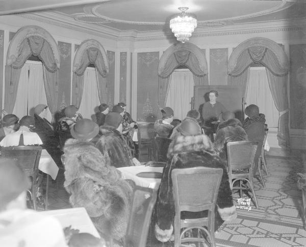 Cecily Weaver teaching a bridge class to large group of well-dressed women at the Loraine Hotel.