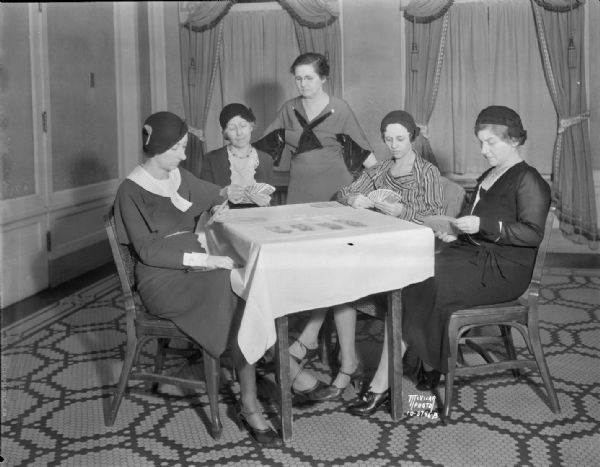 Cecily Weaver teaching bridge and the use of the Fulton Shur-Win Bidder to a table of four women. Sitting left to right are: Esther Hermsen, Inger Emery, Geneva Fosse, and Helen Berkwich.