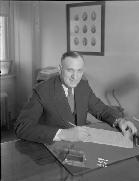 Mayor James R. Law sitting at a desk signing a document in City Hall, 2-4 W. Mifflin Street.