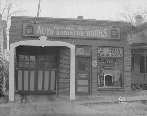 Capital City Auto Radiator Works, 503 E. Washington Avenue, Leo Slavney, proprietor, exterior. Sign above window reads: "Cut Costs with Leo's (Slavney) Radiator Service." The garage door on the left is outlined with a frame that looks like the front of an automobile's radiator.