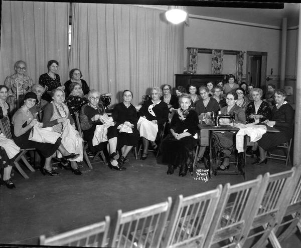 Large group of women sewing for the Red Cross at St. John's Lutheran Church, 322 East Washington Avenue. Shows a woman sitting behind a sewing machine on the right.