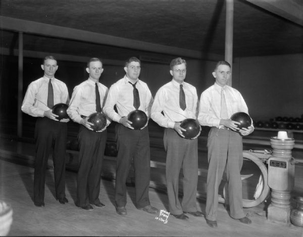 Dean's Office Nite Club (five male students) bowling team, each holding his bowling ball, at the Plaza Bowling Alley, 319 North Henry, left to right: George Kroening, Zenno Gorder, Frank Molinaro, Harold Johnson and Ed Borkenhagen. "Loop the Loop ball return."
