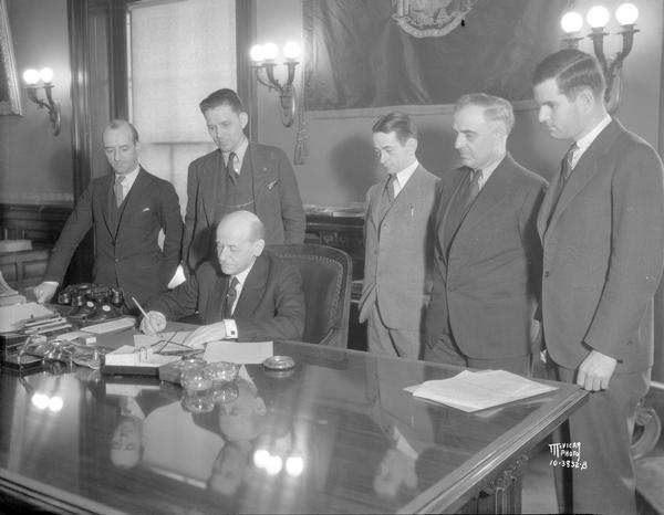 Governor Albert G. Schmedeman signing mortgage bill which grants moratoriums to Wisconsin farm and home mortgages. Left to right:  Senator William Shannors; Arnold Gilberts, state president of the Wisconsin Farm Holiday association; Governor Schmedeman; Assemblyman Willis E. Donley, sponsor of the bill in the Assmenbly; Louis Davalin, legal counsel of the Wisconsin Farm Holiday association; and John Casey, the Governor's legal counsel.