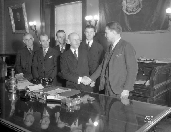 Governor Albert G. Schmedeman shaking hands after signing mortgage bill which grants moratoriums to Wisconsin farm and home mortgages. Left to right are: Senator William Shannors; Arnold Gilberts, state president of the Wisconsin Farm Holiday association; Governor Schmedeman; Assemblyman Willis E. Donley, sponsor of the bill in the Assembly; Louis Davalin, legal counsel of the Wisconsin Farm Holiday association; and John Casey, the Governor's legal counsel.