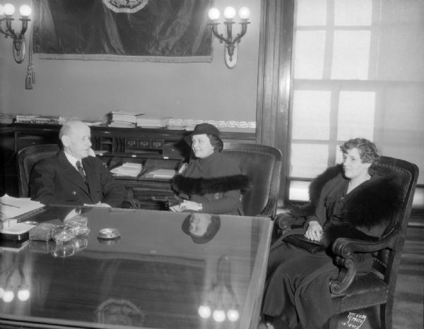 Governor Albert G. Schemedeman with Frieda Mooney, National Commander of the Disabled American Veterans of the World War Auxiliary, and Nina Westbury, National senior vice commander of the auxiliary, sitting in his office, thanking the Governor for D.A.V. aid.